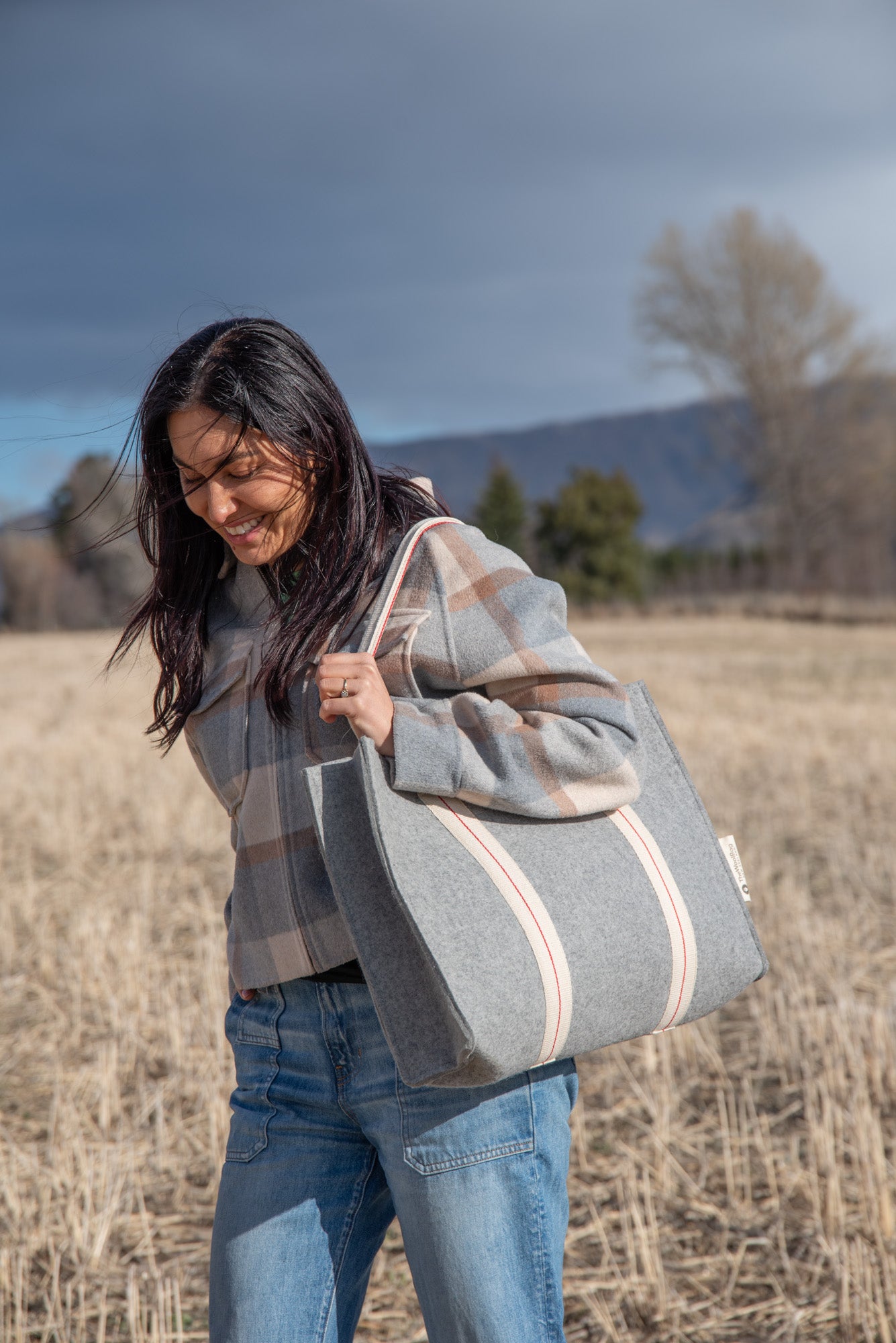 Woman holding a large gray tote bag in an open field with mountains in the background