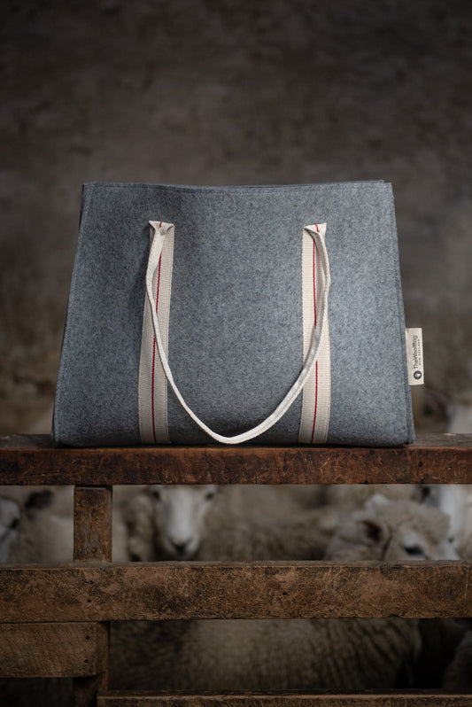 Gray tote bag with striped handles on a wooden surface with sheep in the background