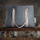 Gray tote bag with striped handles on a wooden surface with sheep in the background